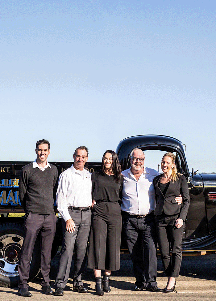 the current five family members and company owners of AH Beard stand smiling before a classic car outdoors after doing a Strategic leadership program.