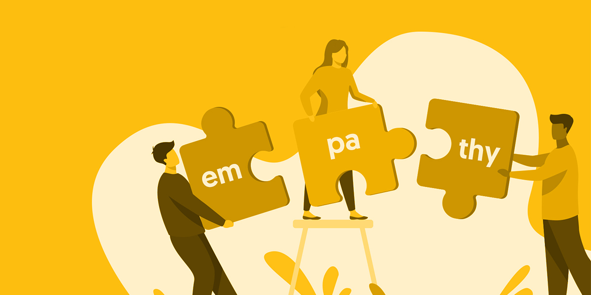 Illustration of three people assembling puzzle pieces that spell the word ‘empathy.’ One person on the left holds the piece with ‘em,’ a person on a step ladder holds the middle piece with ‘pa,’ and another person on the right holds the piece with ‘thy.’ The background is yellow with a large abstract heart shape behind them, symbolising teamwork and compassion.
